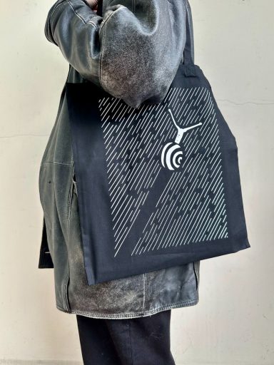 a tote bag designed by the artist of a sold out linocut of a snail racing on a black background, printed in the UK